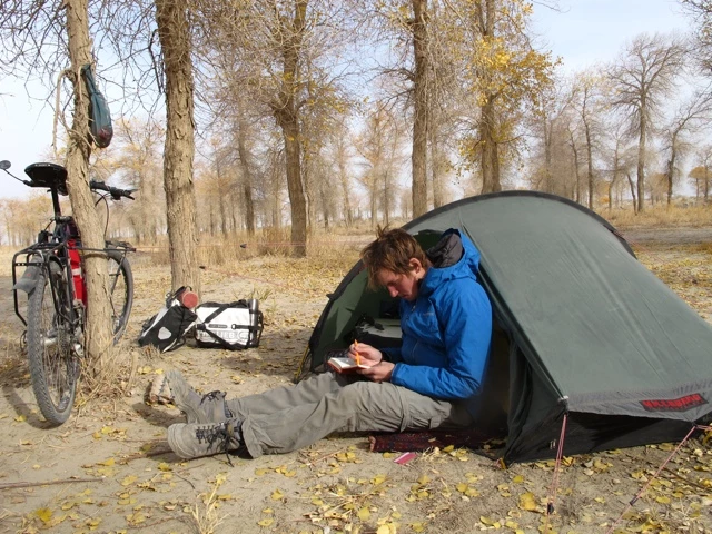 Zeltcamp mit Fahrrad und Gepäck unter kahlen Bäumen, Person sitzt im Zelteingang und macht Pause