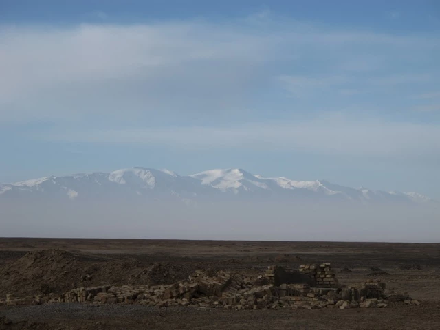 Weite Steppenlandschaft mit felsigem Untergrund, im Hintergrund schneebedeckte Gebirgskette unter blauem Himmel