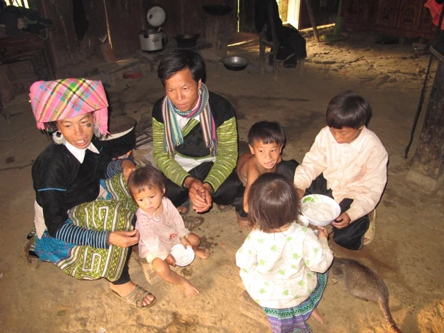 Sechs Menschen in einem Raum, Erwachsene und Kinder in bunten traditionellen Kleidern sitzen auf dem Boden