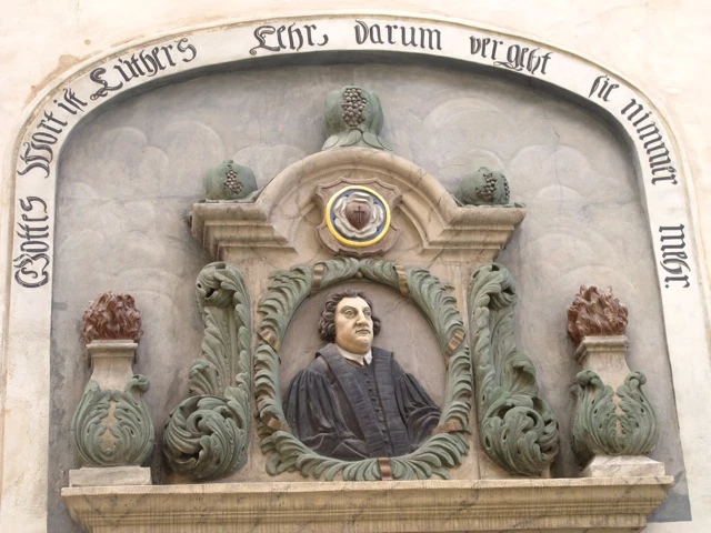 Steinerne Gedenktafel mit barockem Rahmen und Relief eines Mannes in schwarzer Robe, umgeben von ornamentalen Verzierungen
