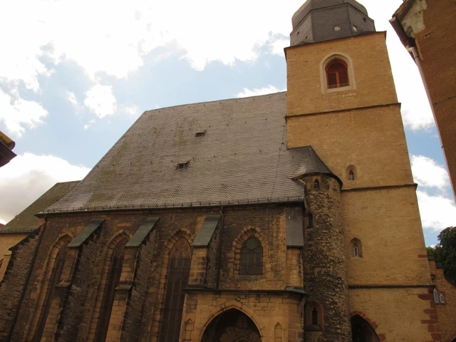 Mittelalterliche Steinkirche mit gotischen Bögen, gelber Fassade und hohem Turm, bewölkter Himmel im Hintergrund