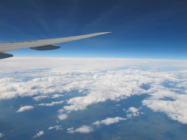 Flugzeugflügel über weißem Wolkenmeer, blauer Himmel und Horizont, Blick aus Passagierflugzeug