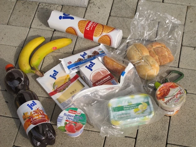 Verschiedene Lebensmittel auf Pflastersteinen: Bananen, Brot, Cola-Flasche, Milchprodukte und Verpackungen