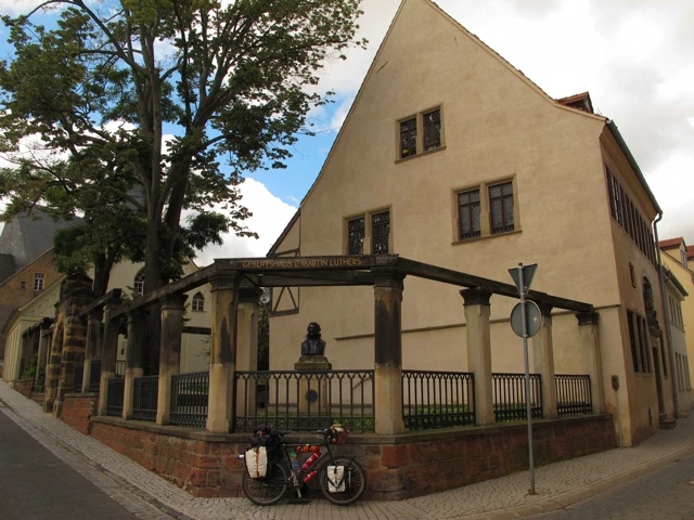 Gelbes Altstadthaus an Strassenecke mit zwei geparkten Fahrrädern, Metallzaun und Baum im Hintergrund